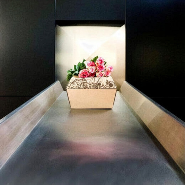 Eine dekorierte Kremationsurne mit rosa Blumen steht auf einem Metallband, wahrscheinlich im Aurora Tierkrematorium. Aurora Tierkrematorium